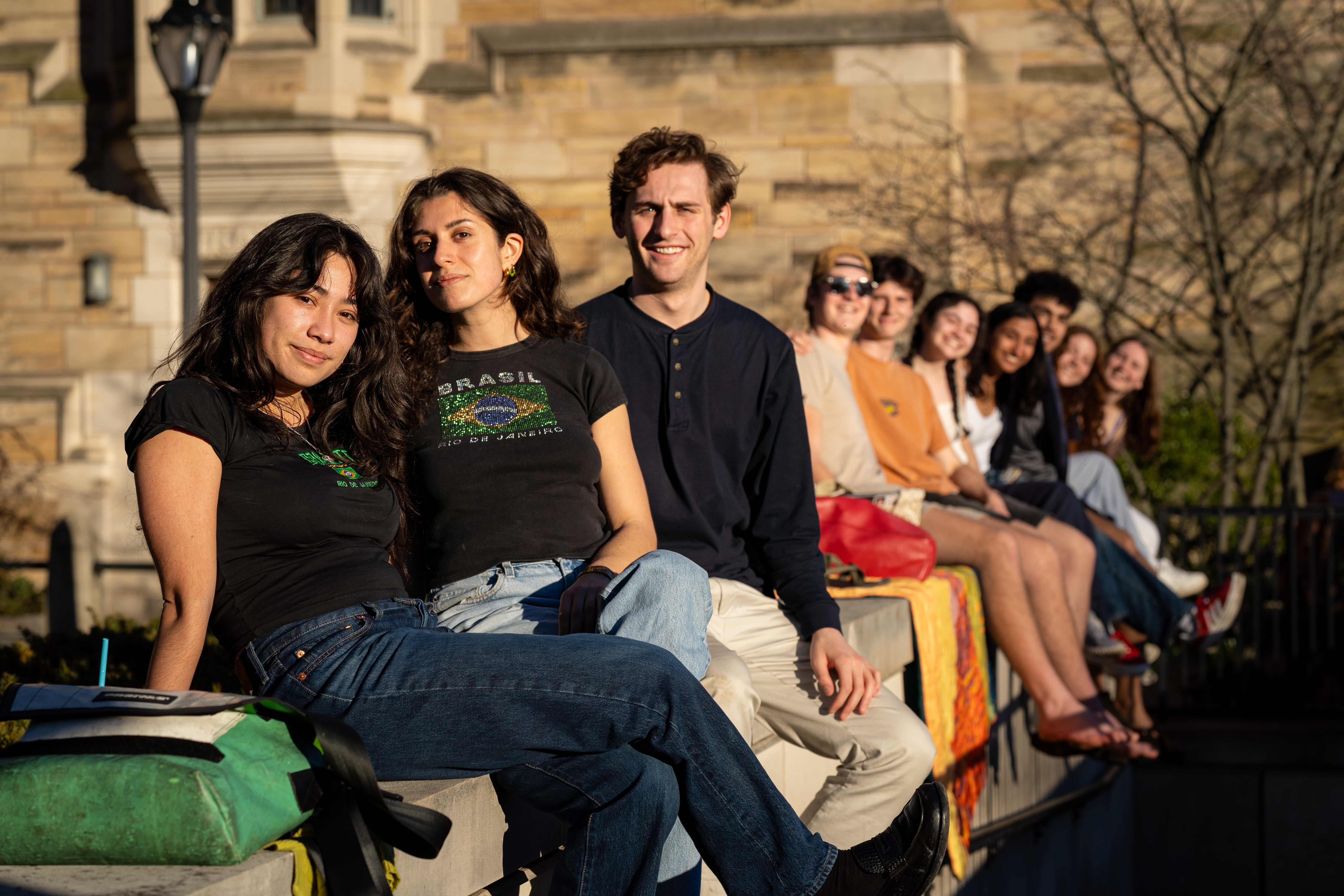 Students lined up sitting on a stone ledge during sunset