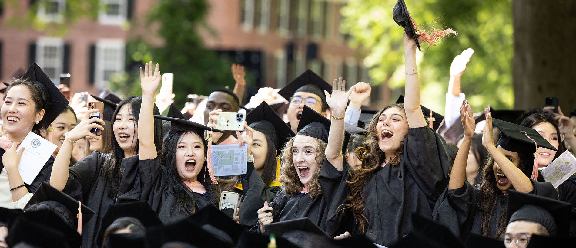 Yale grads in cap and gown in front of the entrance arch, tossing their caps